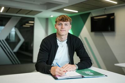 Paul Bellmann sitzt vor der Werder-Raute und unterschreibt seinen Vertrag.