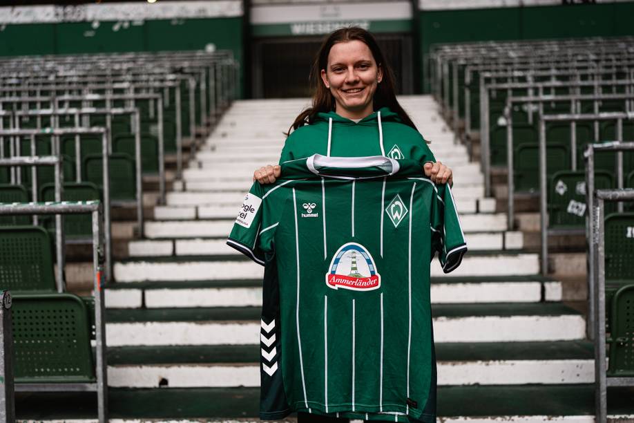 Sarah Ernst steht in der Ostkurve und hält das Werder-Heimtrikot hoch.
