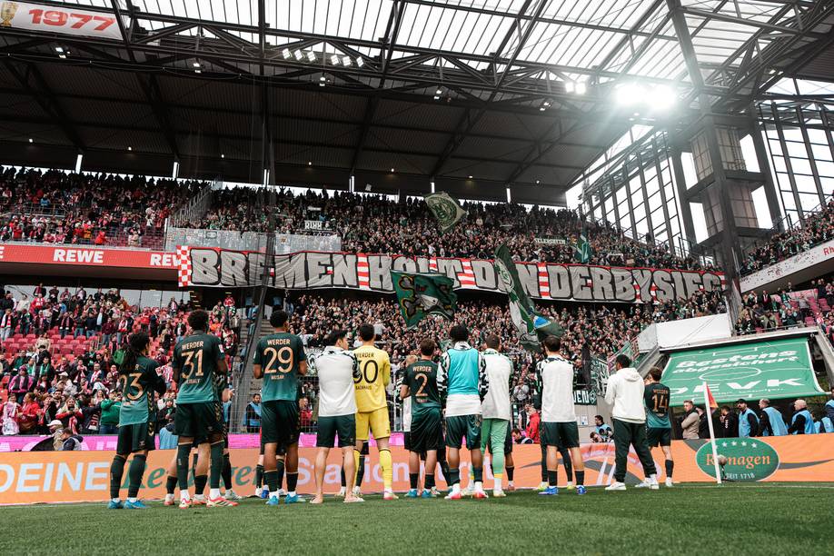 Die Mannschaft steht vor der Gästekurve, auf einem Transparent steht: Bremen holt den Derbysieg!