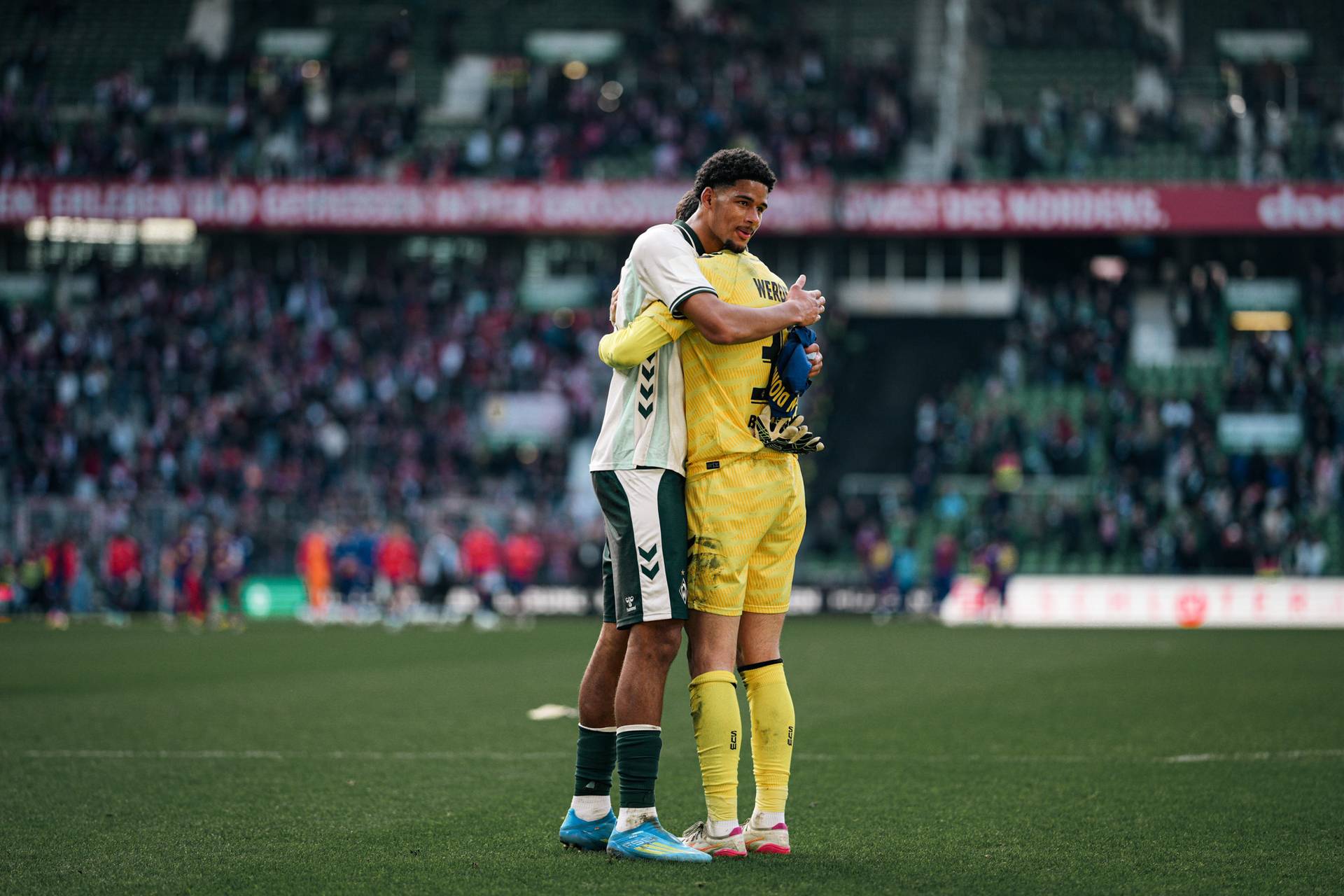Salim Musah umarmt Mio Backhaus, in der Hand trägt er ein Trikot von Yan Diomande.
