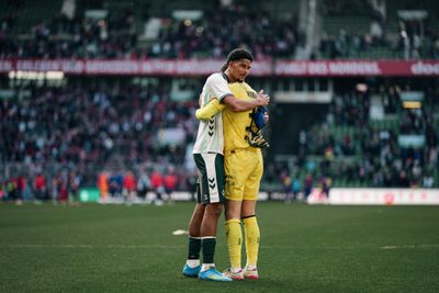 Salim Musah umarmt Mio Backhaus, in der Hand trägt er ein Trikot von Yan Diomande.