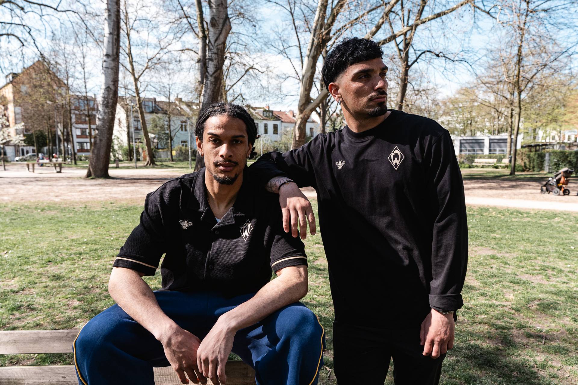 Isaac Schmidt links im schwarzen Werder-Kurzarmhemd von hummel und rechts Cameron Puertas im schwarzen Werder Sweatshirt von hummel auf einem Spielplatz