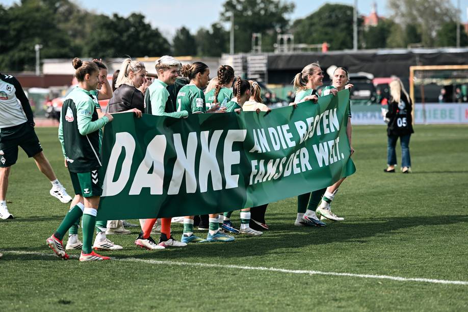 Fußballspieler auf dem Spielfeld halten ein Transparent mit einer Dankesbotschaft an die Fans, die auf Deutsch verfasst ist.