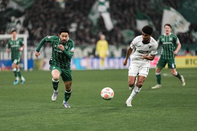 Yukinari Sugawara chases after the ball, next to a TSG player.