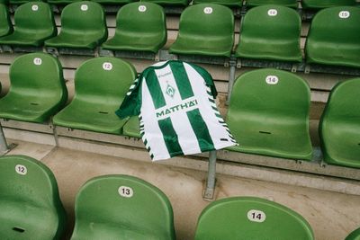 Ein grün-weiß gestreiftes Fußballtrikot, das über einem Sitz mit dem „MATTHÄI“-Logo drapiert ist, umgeben von nummerierten grünen Stadion-Sitzen.