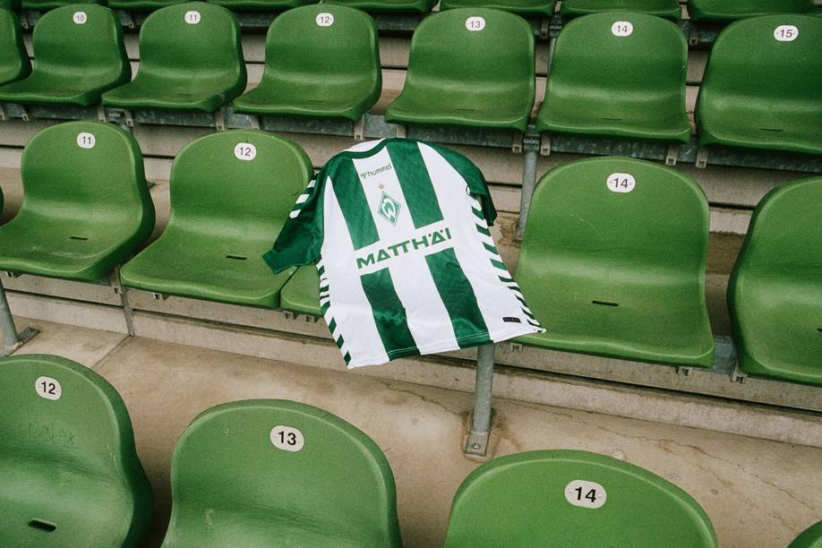 Ein grün-weiß gestreiftes Fußballtrikot, das über einem Sitz mit dem „MATTHÄI“-Logo drapiert ist, umgeben von nummerierten grünen Stadion-Sitzen.
