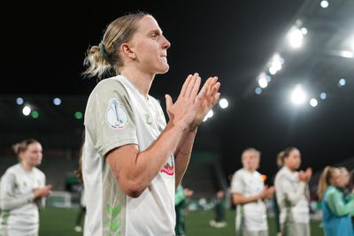 Fußballspieler in einem weißen Trikot klatscht auf dem Spielfeld, im Hintergrund stehen seine Teamkollegen unter den hellen Stadionlichtern.