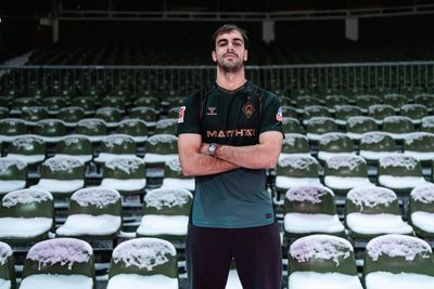 Jovan Milosevic steht mit verschränkten Armen auf einer Tribüne mit schneebdeckten Sitzen im Weserstadion.