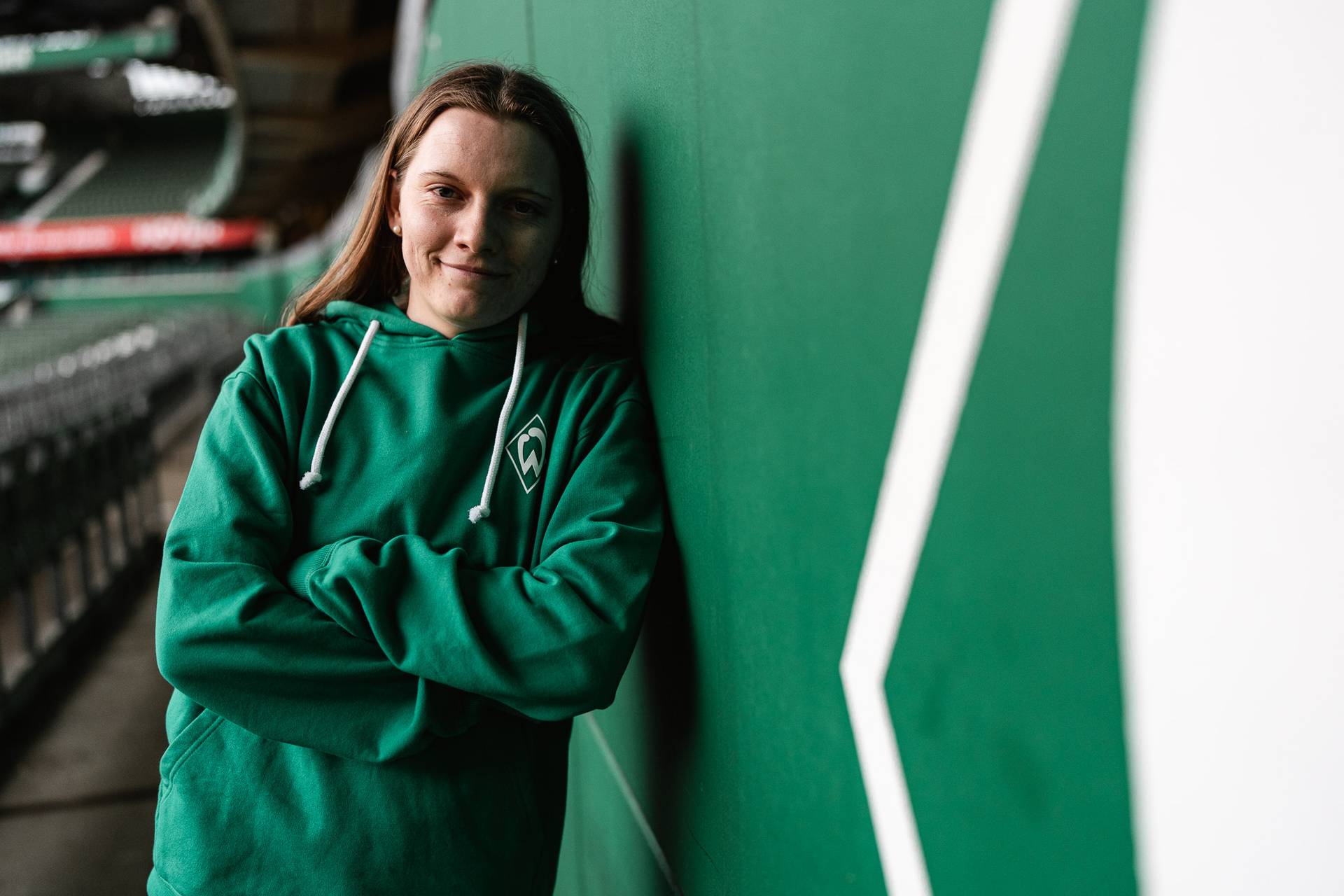 Sarah Ernst in Großaufnahme. Sie lehnt an der Ostkurvenwand und trägt einen grünen Werder-Hoodie.