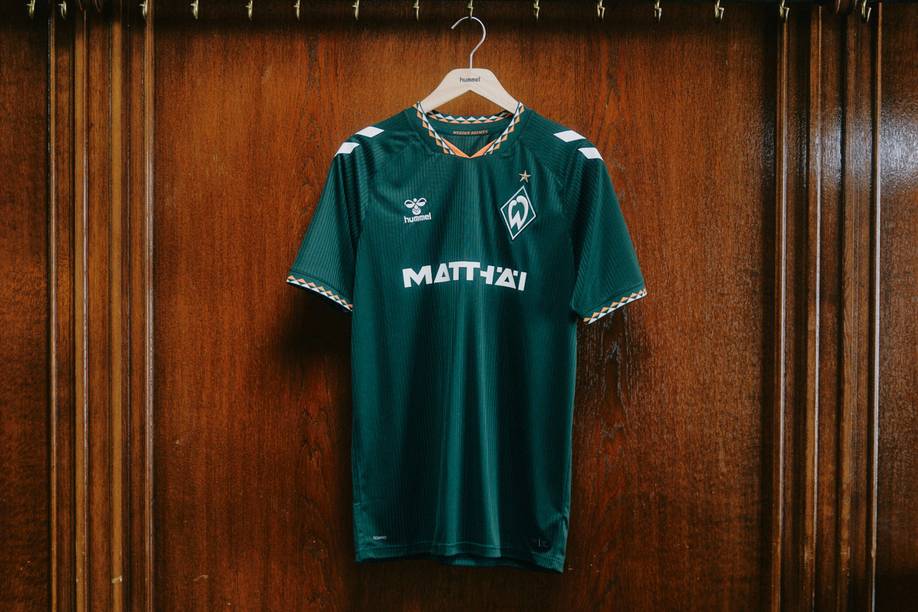 Grünes Sporttrikot mit einem Logo und der Aufschrift „MATTHÄI“, das an einer Holzplatte aufgehängt ist.