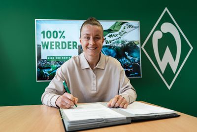 Michelle Ulbrich sitzt an einem Tisch, vor ihr liegt ein Ordner mit Dokumenten, in ihrer rechten Hand hält sie einen Stift.