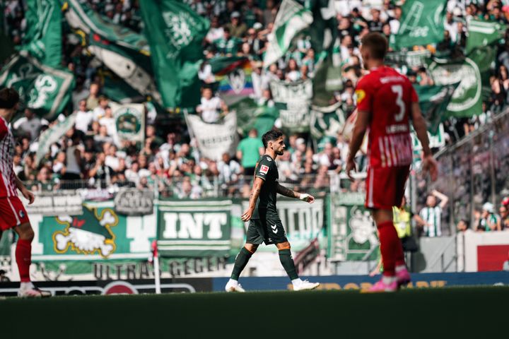 Ludovit Reis geht über den Platz, im Hintergrund der Gästeblock.