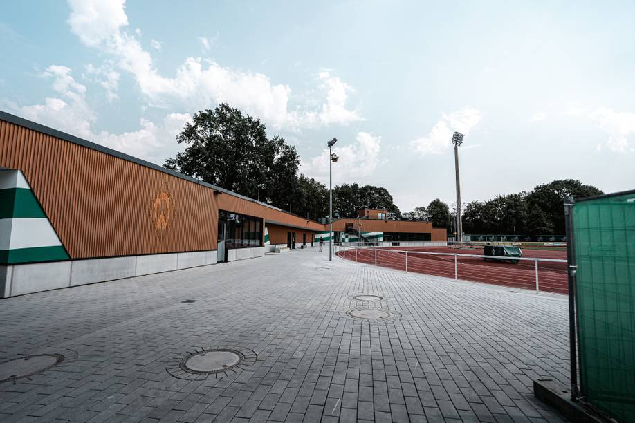 Eine moderne Sportanlage mit einer Laufbahn, umgeben von Bäumen, unter einem teilweise bewölkten Himmel.