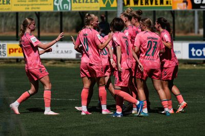 Eine Frauenfußballmannschaft in rosa Trikots versammelt sich auf einem Rasenplatz und feiert während eines Spiels.