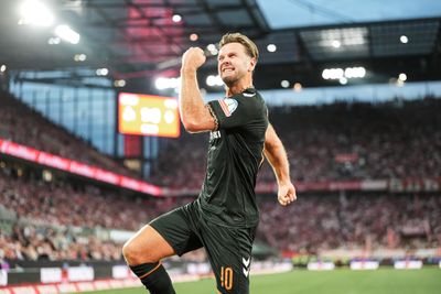 Ein Fußballspieler in einem schwarzen Trikot feiert während eines Spiels in einem vollbesetzten Stadion leidenschaftlich mit geballter Faust.
