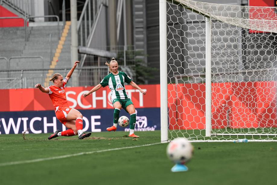 Zwei Fußballspieler gegnerischer Mannschaften kämpfen während eines Spiels auf einem Rasenplatz in der Nähe des Torpfostens um den Ball.