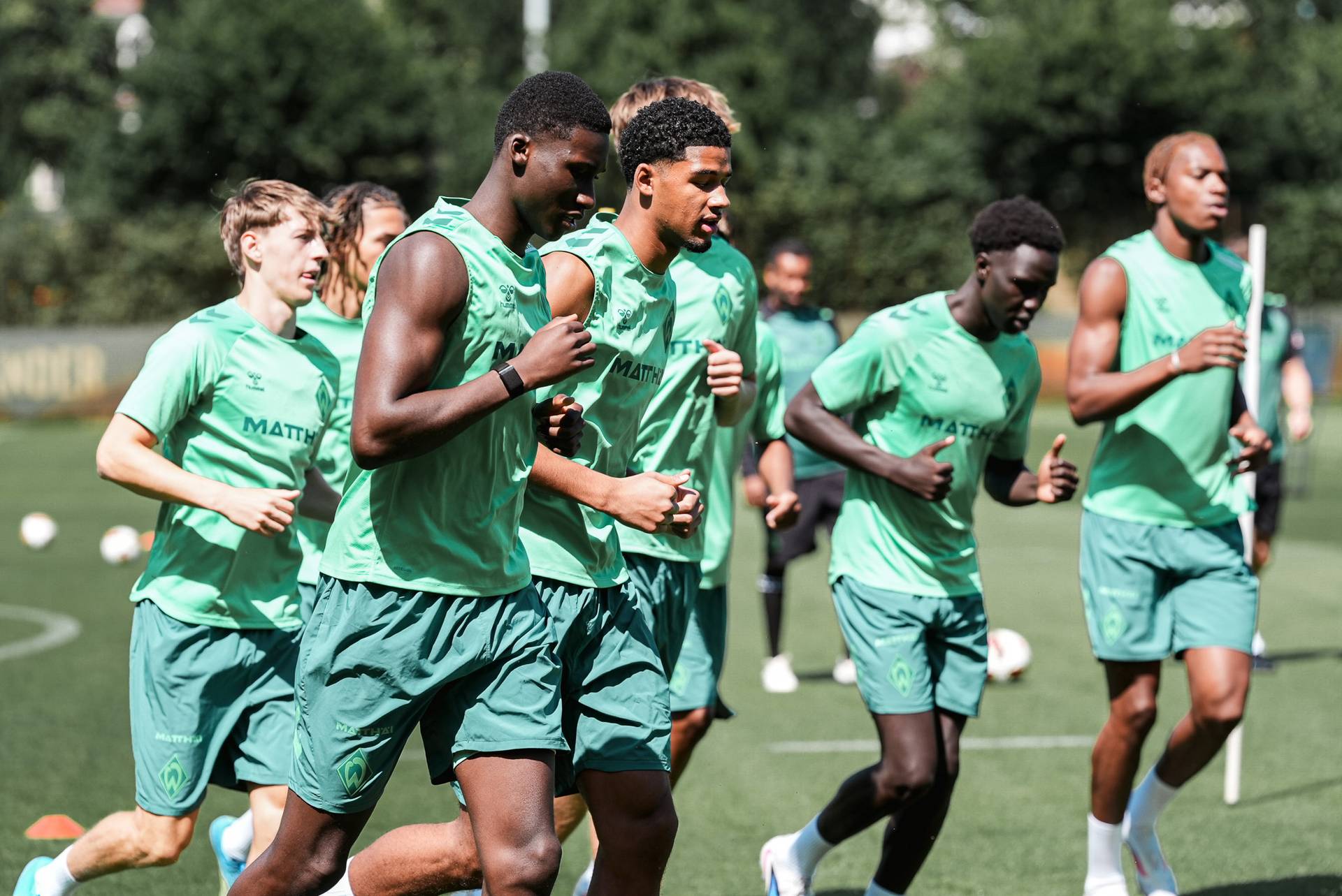 Eine Gruppe von Fußballspielern in grünen Trikots und Shorts, die während einer Trainingseinheit auf einem Rasenplatz joggen.