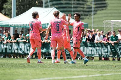 Fußballspieler in rosa Trikots klatschen sich auf dem Spielfeld ab, im Hintergrund ist eine Zuschauermenge zu sehen; sie tragen Trikots mit den Aufschriften „Werder“, „Stage“ und Rückennummern.