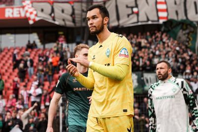Ein Fußballspieler im gelben Trikot klatscht auf dem Spielfeld, im Hintergrund sind seine Mannschaftskameraden und die Zuschauer zu sehen, Stadionbanner sind zu erkennen.