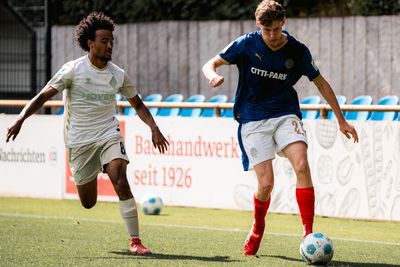 Zwei Fußballspieler kämpfen auf einem Rasenfeld um den Ball, wobei einer ein Werder Trikot und der andere ein Kiel Trikot trägt.