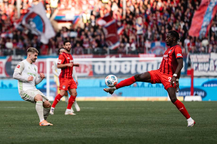 Ein Heidenheimer Spieler streckt das Bein um an den Ball zu kommen, Romano Schmid läuft auf ihn zu.