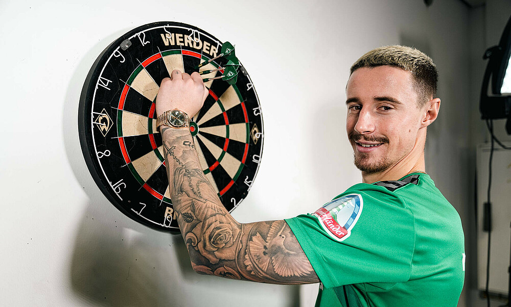 null Friedl steht an der Dartscheibe.