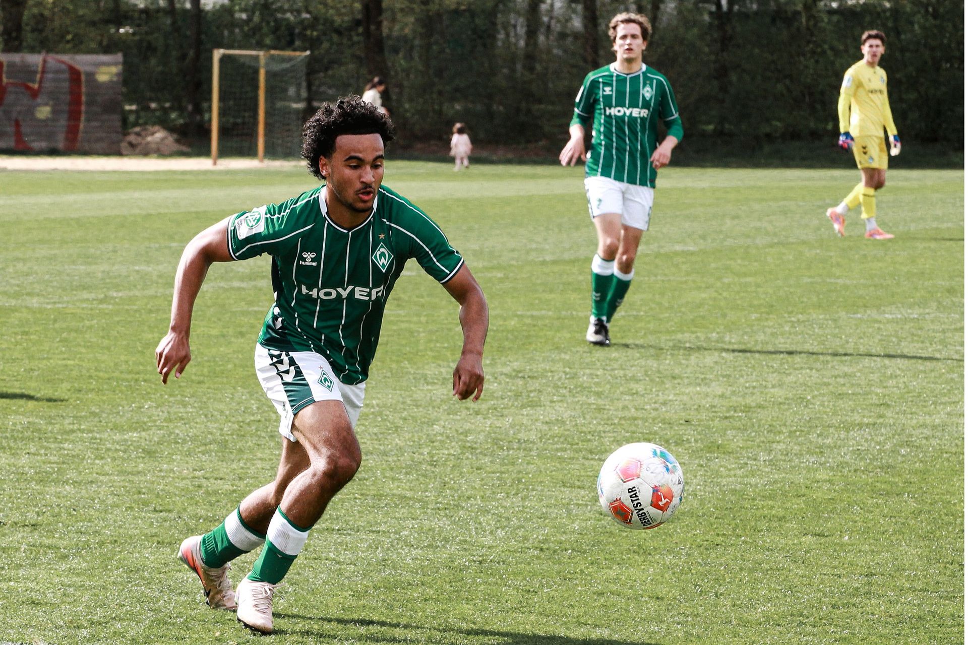 Ein Spieler der Werder-U19 im grün-weißen Dress läuft mit dem hochspringendem Ball in Richtung der rechten Bildhälfte