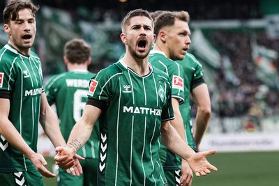 Fußballspieler in grünen Trikots reagieren leidenschaftlich auf dem Spielfeld, wobei ein zentraler Spieler während eines Spiels eindringlich gestikuliert.