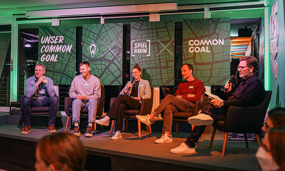 Das Foto zeigt die Podiumsdisskusion mit 5 Teilnehmenden auf der Bühne.
