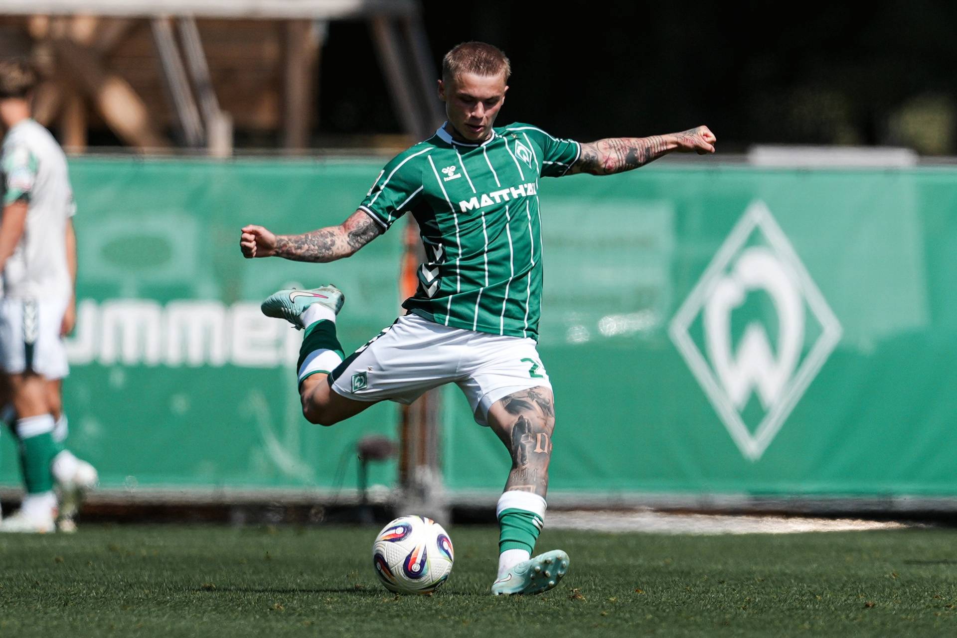 Isak Hansen-Aarøen is wearing a green and white shirt and white shorts. He is preparing to strike the football in front of him.