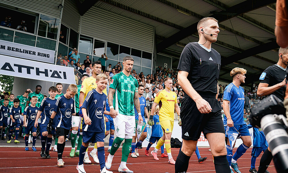 Friedl und Werder-Spieler laufen zusammen mit Spielern des FC Verden 04 ein.