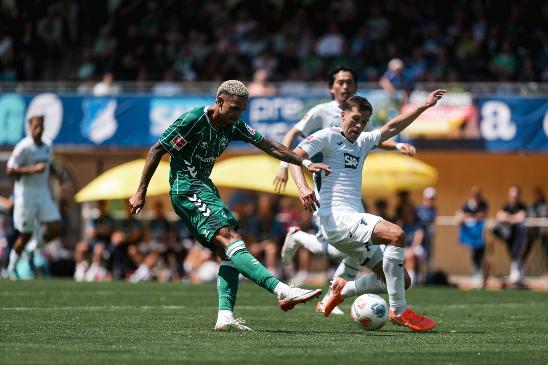 Justin Njinmah holt zum Schuss aus, neben ihm versucht ein Hoffenheimer das zu verhindern.