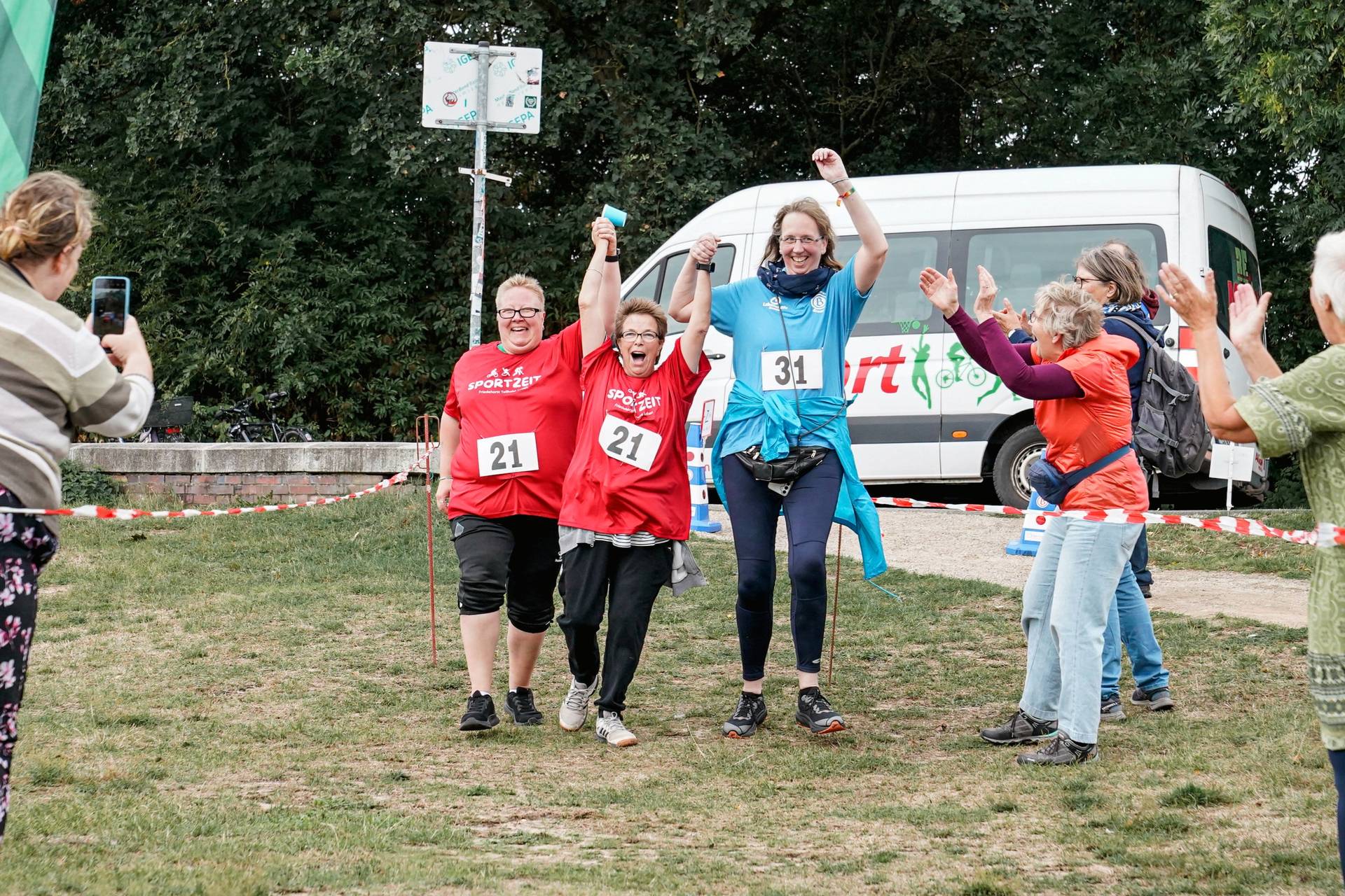 Drei Frauen laufen Hand in Hand ins Ziel.