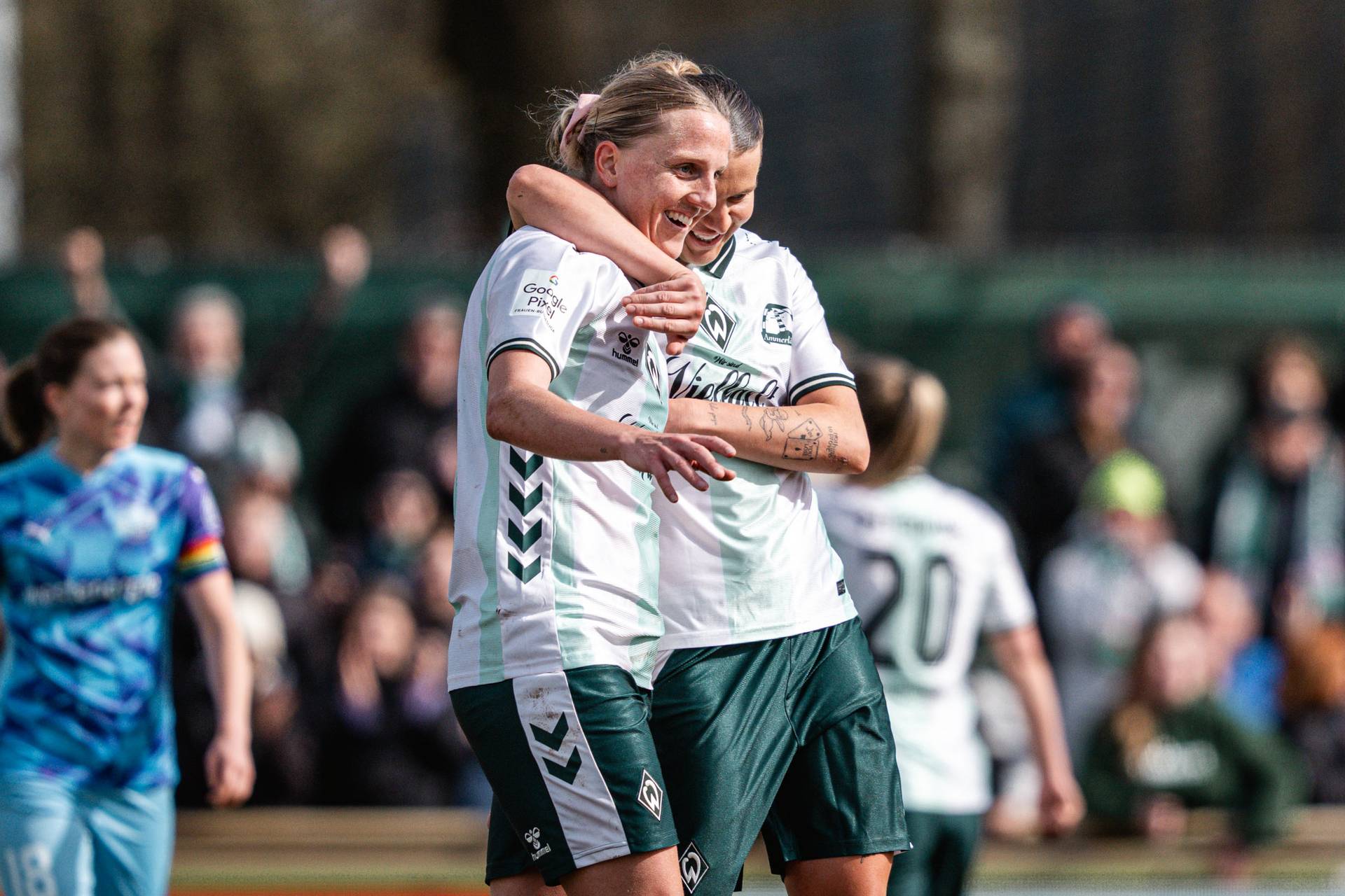 Lina Hausicke im weißen Trikot und grüner Hose lacht. Larissa Mühlhaus hat einen Arm um ihren Hals gelegt.