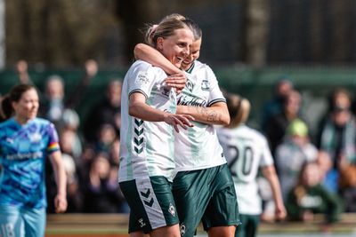 Lina Hausicke im weißen Trikot und grüner Hose lacht. Larissa Mühlhaus hat einen Arm um ihren Hals gelegt.