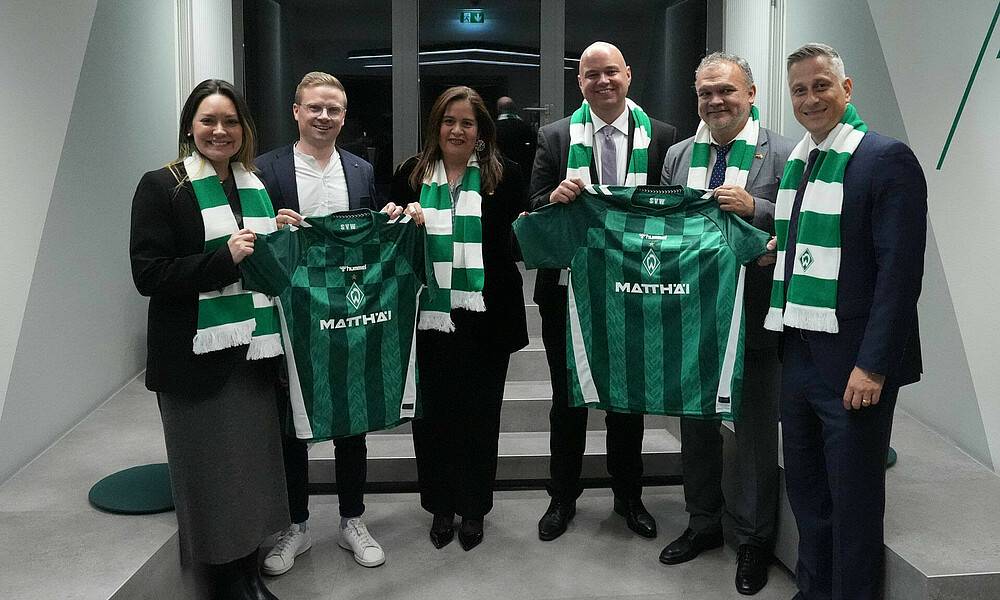 Mehrere Personen stehen zusammen und halten Werder-Trikots hoch