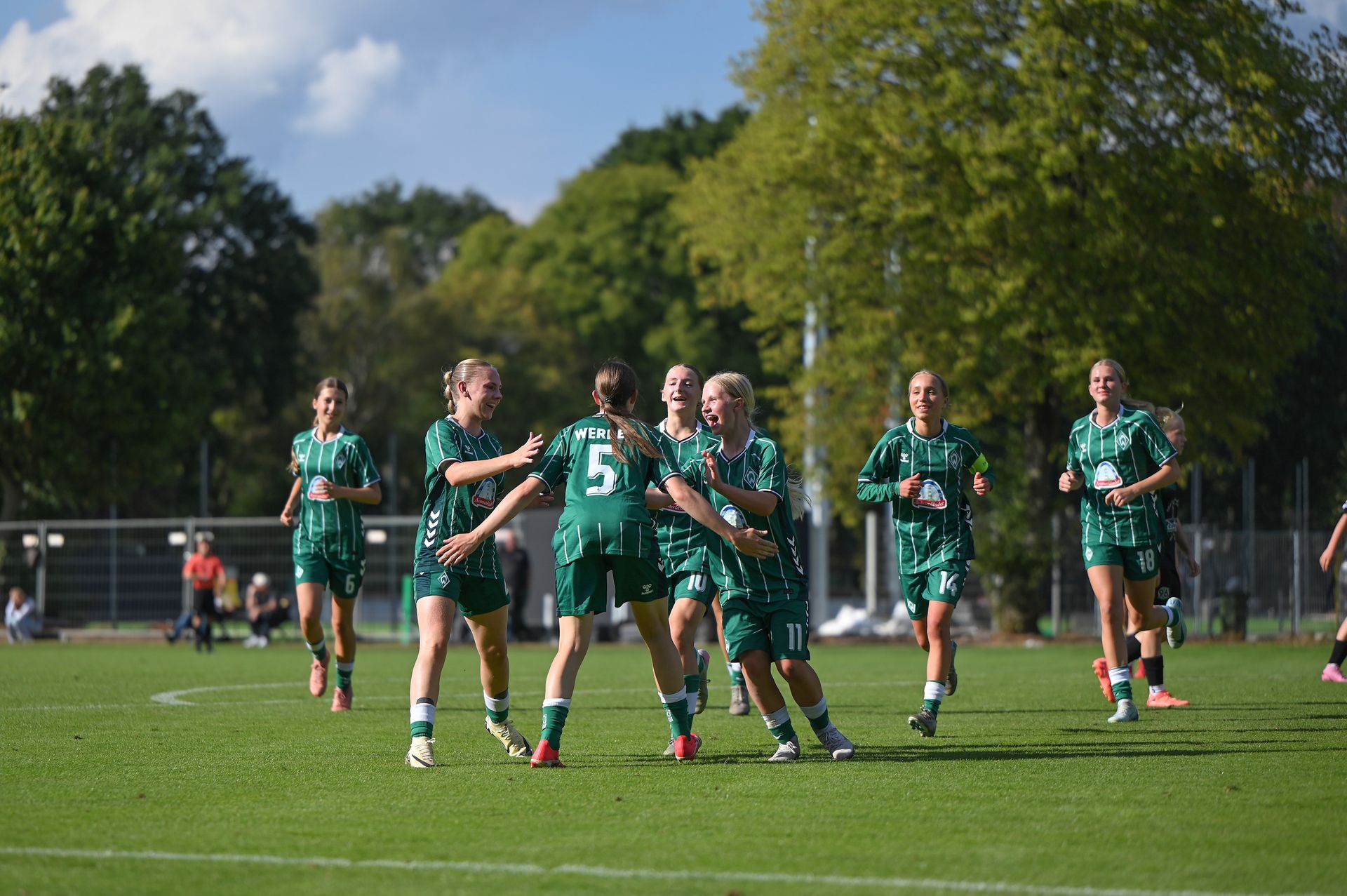 Die U17 in grünen Trikots jubelt auf dem Platz bei sonnigem Wetter.