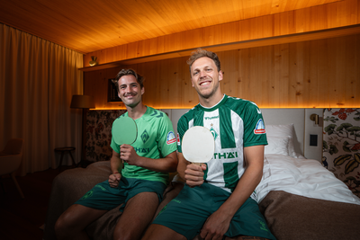 Olivier Deman und Senne Lynen halten beim Zimmerduell Tischtennisschläger hoch und lachen in die Kamera.