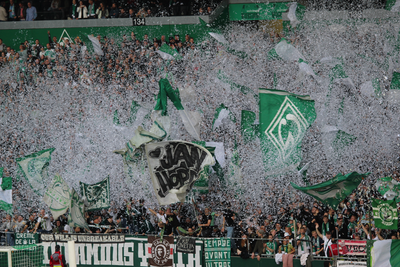 Die Bremer-Ostkurve im Weserstadion. Zu sehen: ein grün-weißes Fahnenmeer und weißes Konfetti.