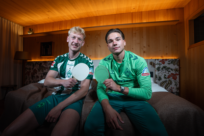 Oskar Wojcik und Dariusz Stalmach sitzen im Hotel auf dem Bett und halten Tischtennisschläger in die Kamera.