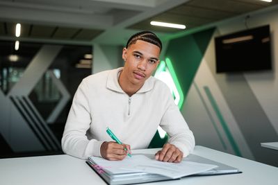 Jasha Barry sitzt an einem Schreibtisch und unterschreibt einen Vertrag.