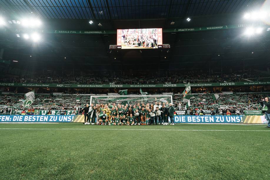 Die Mannschaft der Werder-Frauen steht gemeinsam vor dem Tor vor der mit Fans gefüllten Ostkurve.