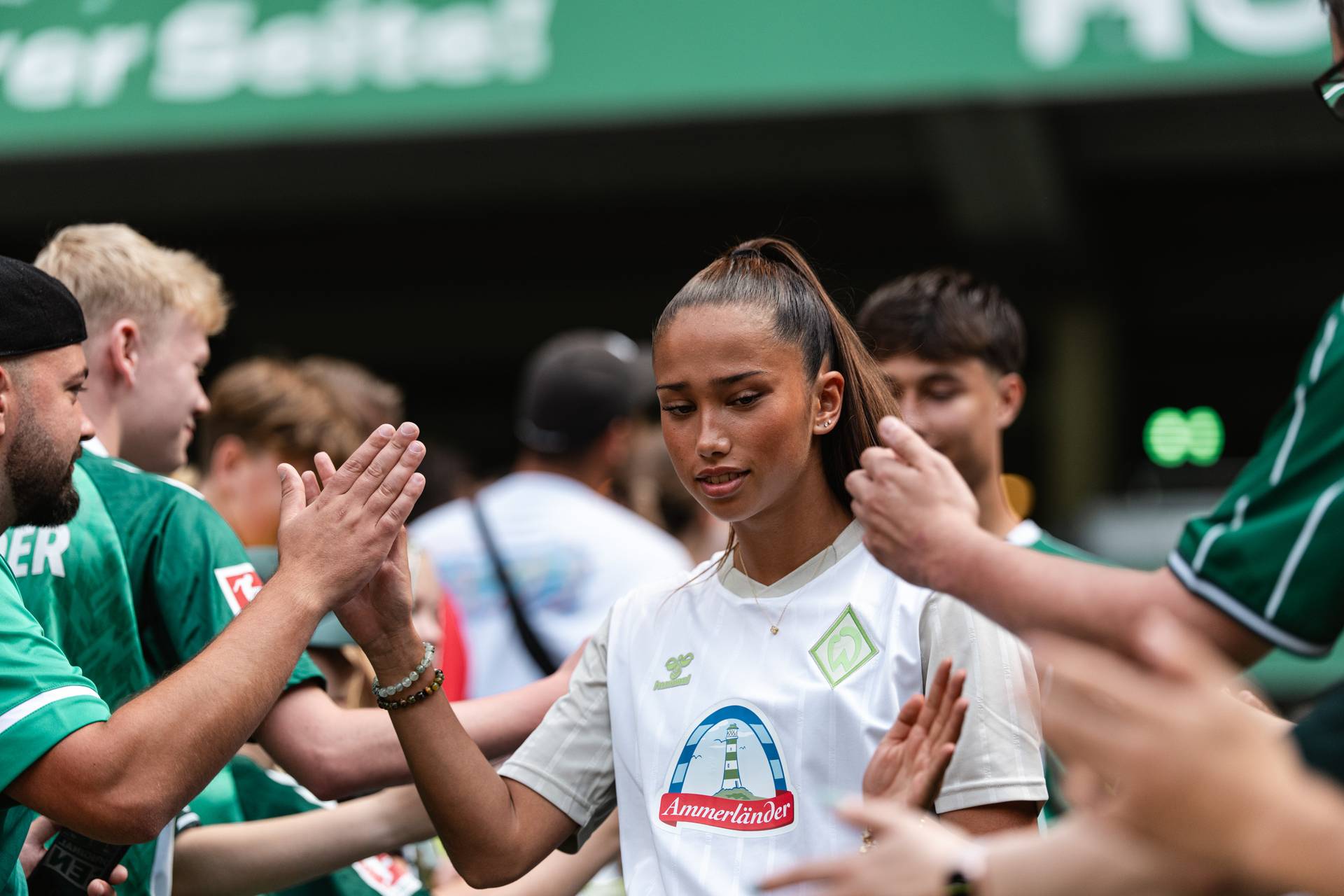 Amira Dahl in einem weißen Sporttrikot gibt den Fans in einem Stadion, umgeben von Menschen in grünen Trikots, ein High-Five.