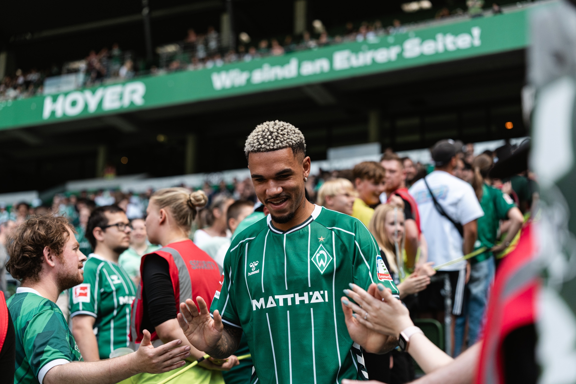 Ein Fußballspieler in einem grünen Trikot gibt den Fans in einem vollbesetzten Stadion mit einem zufriedenen Gesichtsausdruck ein High-Five.
