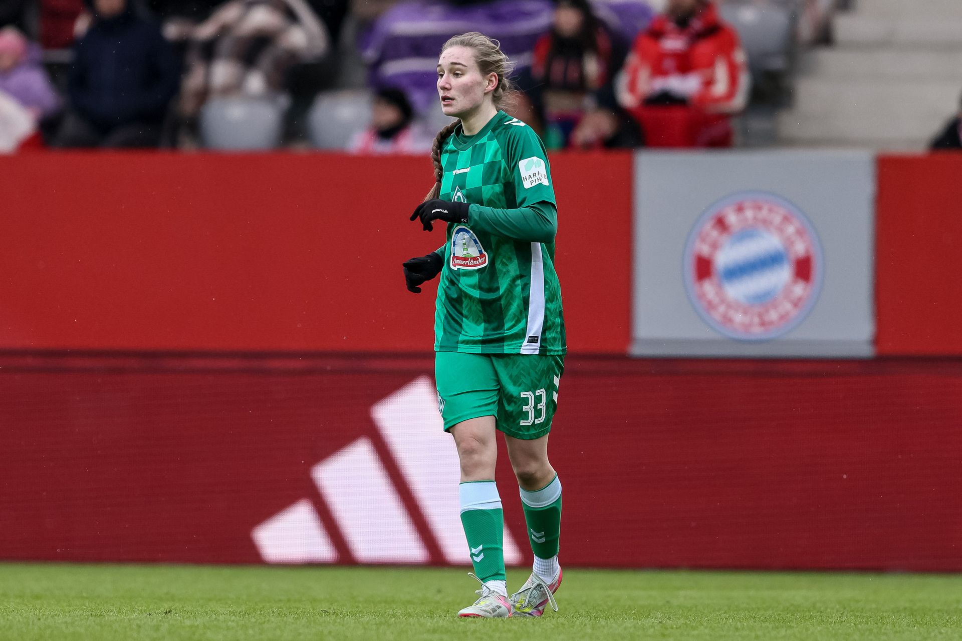 Maria Penner in grüner Uniform steht während eines Spiels auf dem Spielfeld, im Hintergrund verschwommene Zuschauer und eine rote Absperrung.