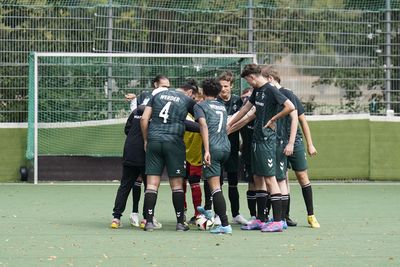Eine Fußballmannschaft steht auf einem grünen Feld in dunklen Trikots mit weißen Akzenten in der Nähe eines Tores mit einem grünen Netz.