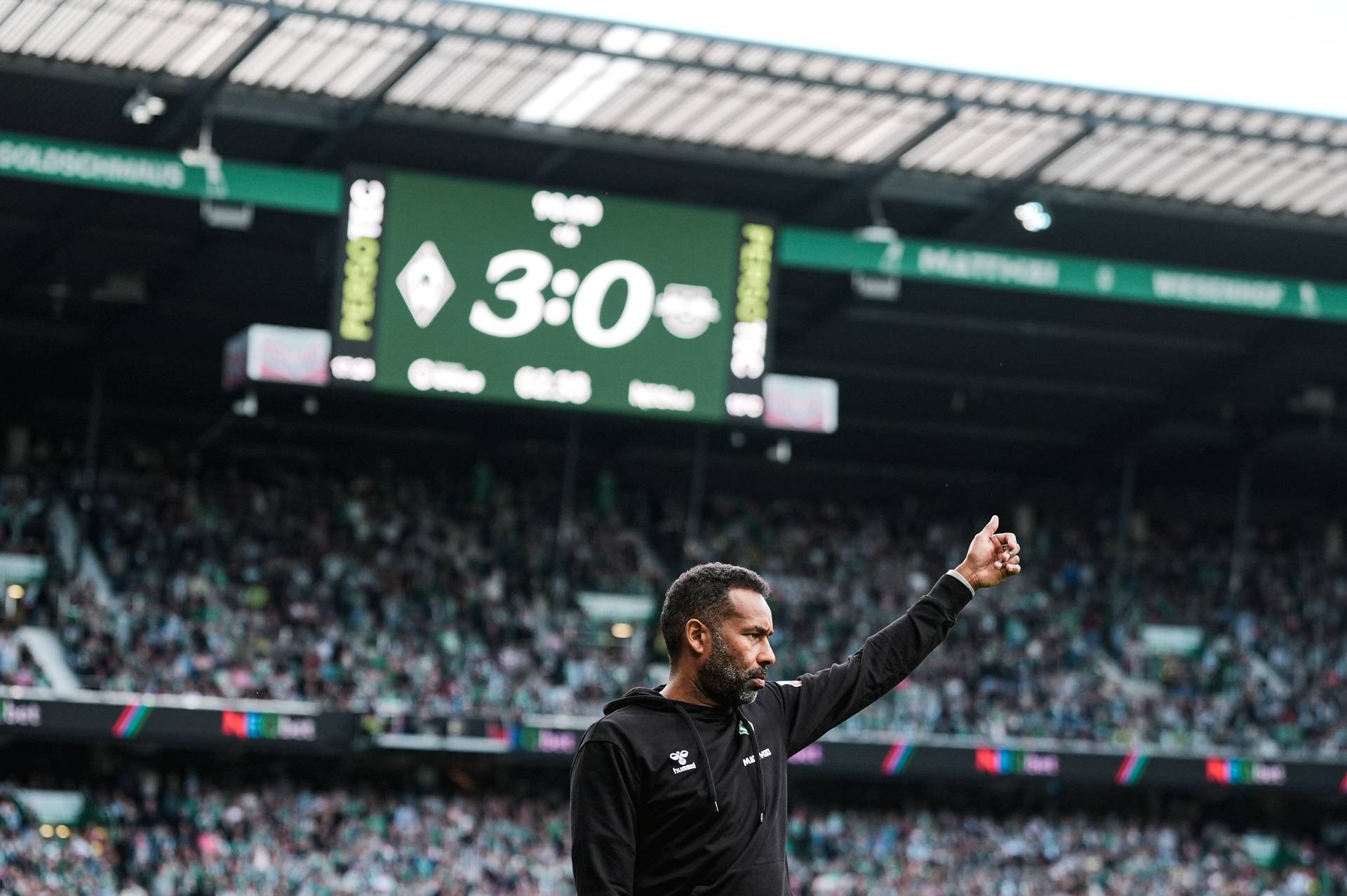 Daniel Thioune zeigt einen Daumen hoch im Weserstadion. Im Hintergrund sieht man die Anzeigetafel des Weserstadions die den Spielstand anzeigt: Werder - Leipzig 3:0.