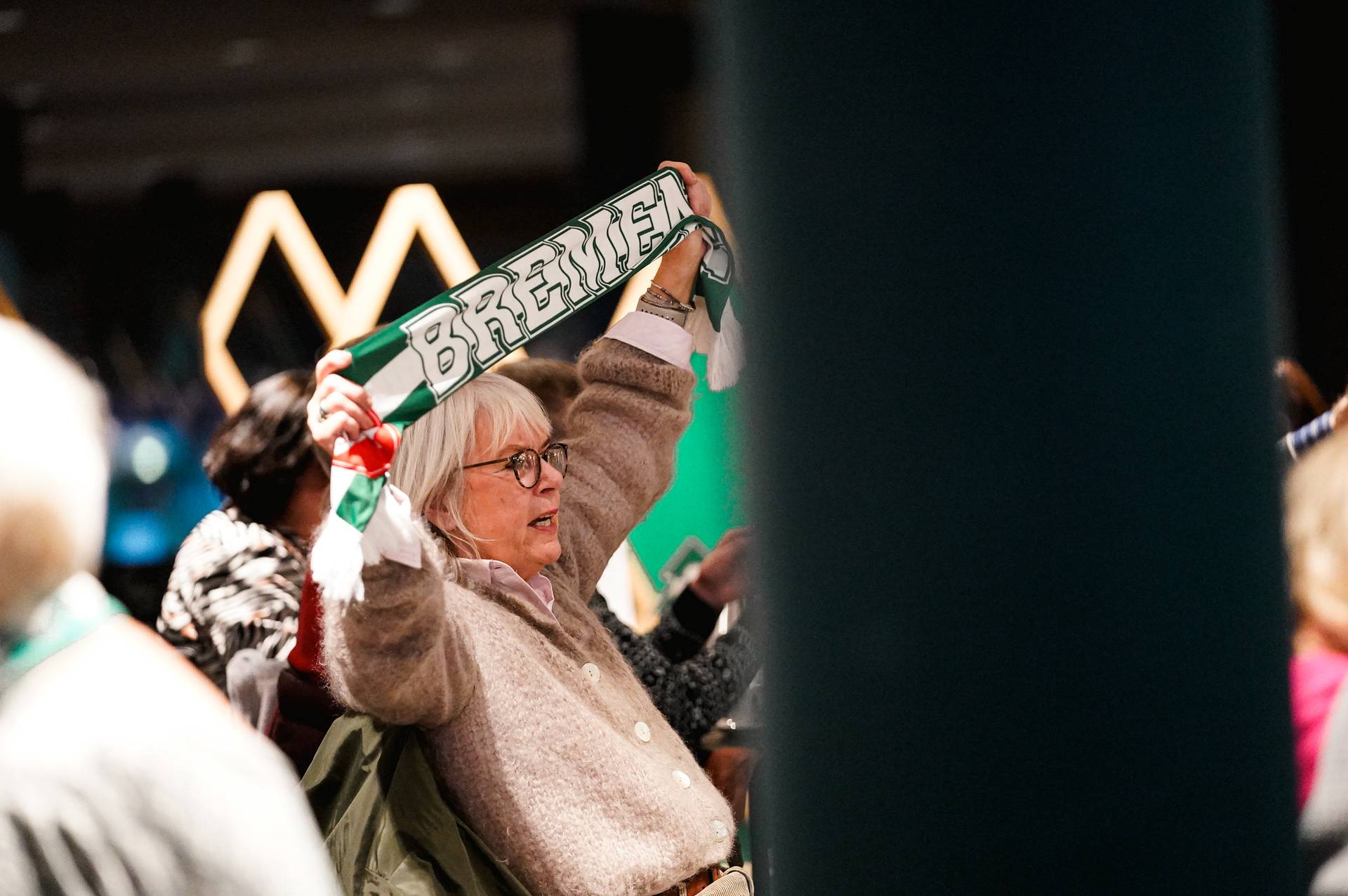 Ein Mitglied von 60plus hält den Werderschal hoch und singt das Lied "Lebenslang Grün-Weiß" mit.