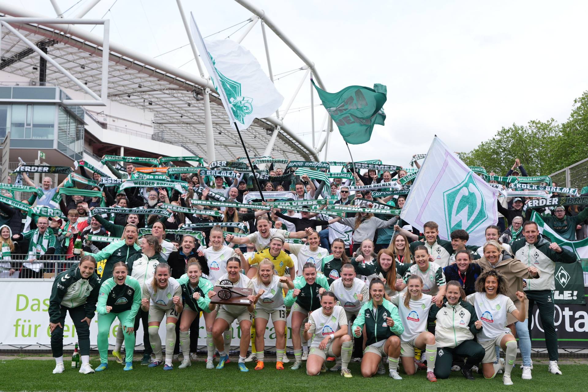 Die WERDERFRAUEN machen ein Siegerbild mit den Fans im Hintergrund.
