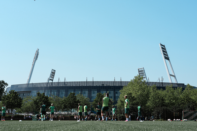 Der Trainingsplatz voller Werder-Spieler. Im Hintergrund ist das Weserstadion bei klarem, blauen Himmel zu sehen.
